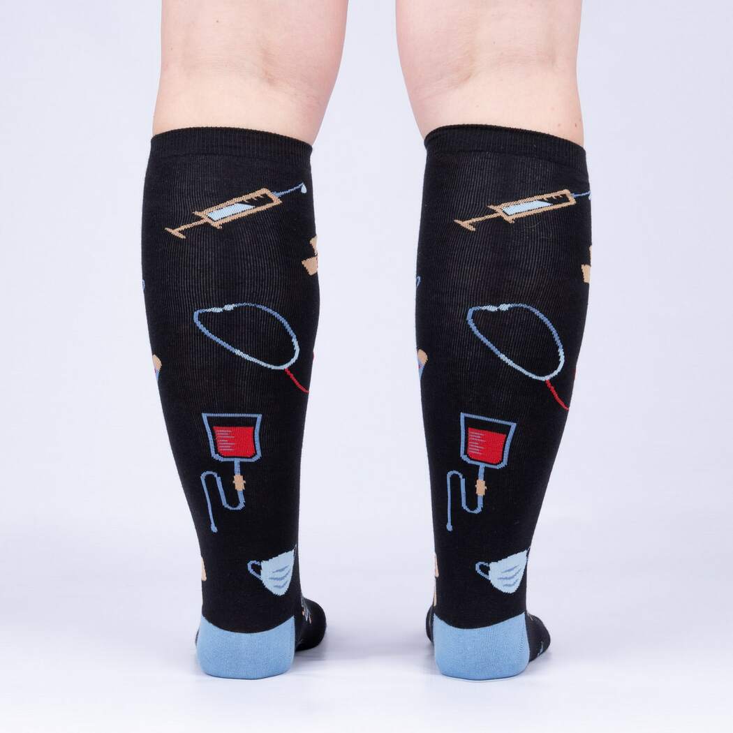 Back view of model wearing the medical knee high socks showing syringes, stethoscopes, and blood bags up the calf