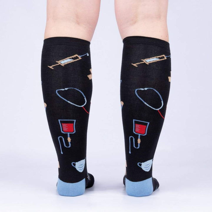 Back view of model wearing the medical knee high socks showing syringes, stethoscopes, and blood bags up the calf