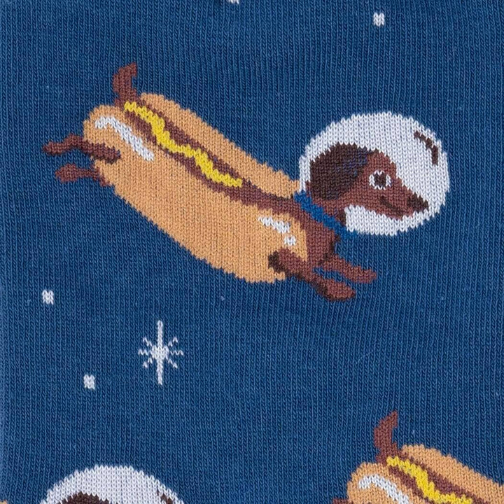 Close-up of a dachshund in a hot dog bun and astronaut helmet floating against a starry navy background